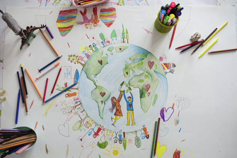 piece of paper with colored pencils on it and a drawing of the earth with people