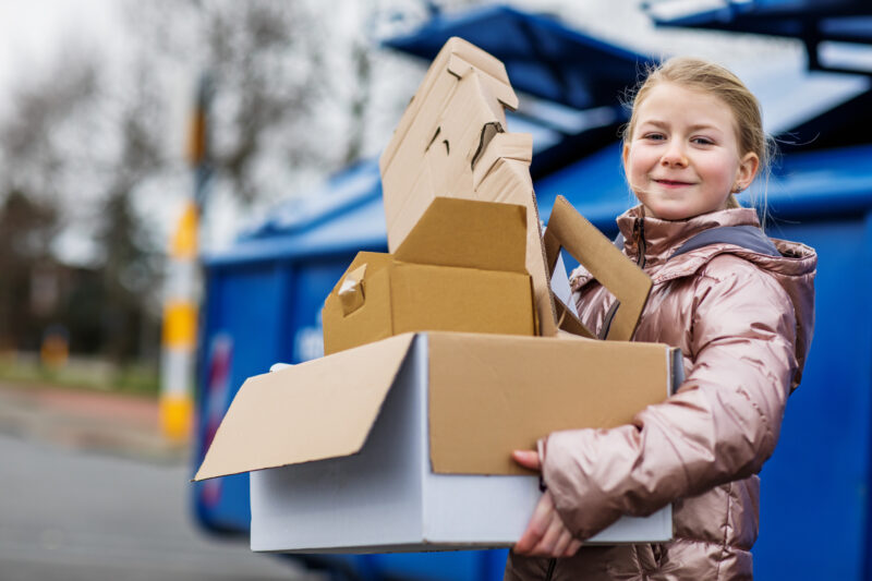 white blonde girl in pink winter coat carrying cardboard boxes