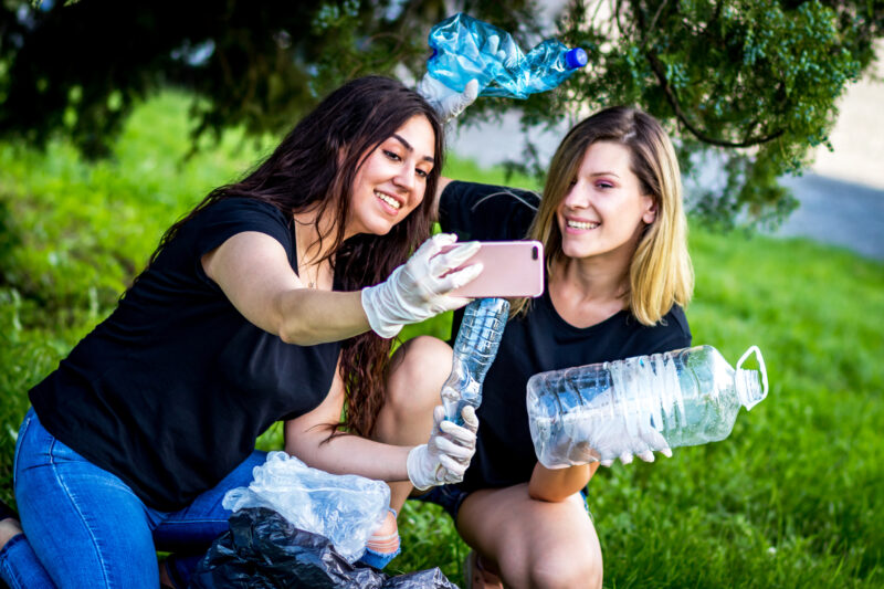 two teen girls taking selfie while recycling plastic bottles